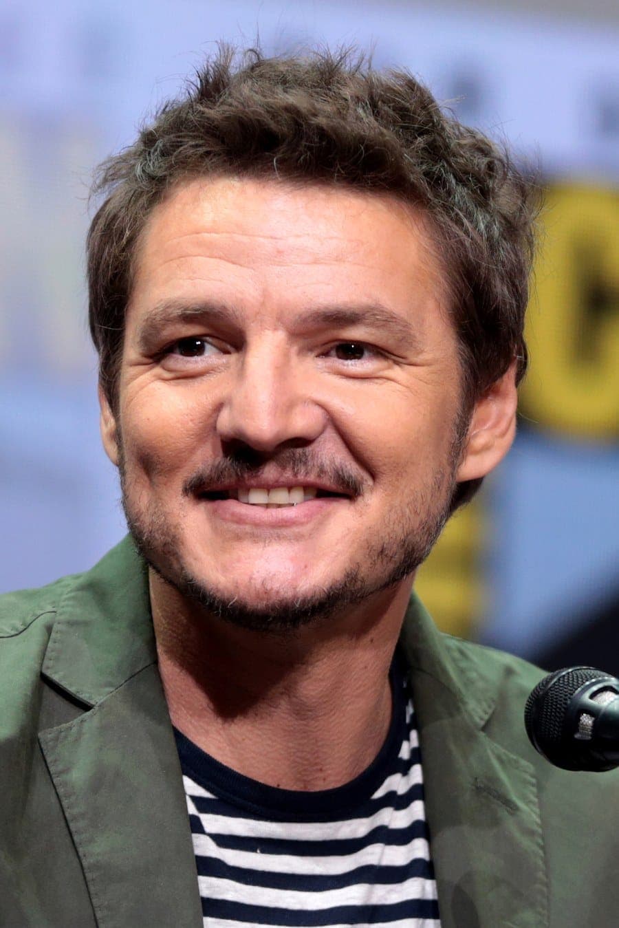 Frontal energy — salt-and-pepper frame, soft smile, warm midface under event light.